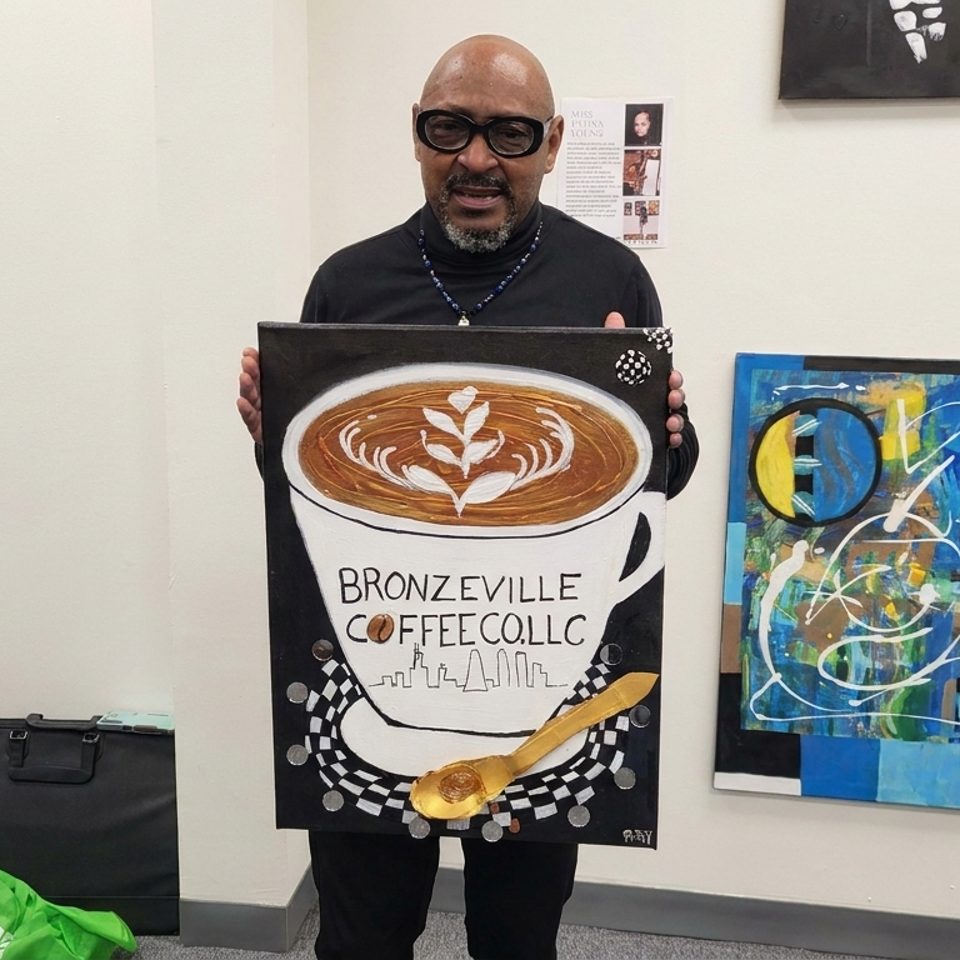 Man wearing glasses holds a painting of a latte cup labeled Bronzeville Coffee Collective in an art-filled room.